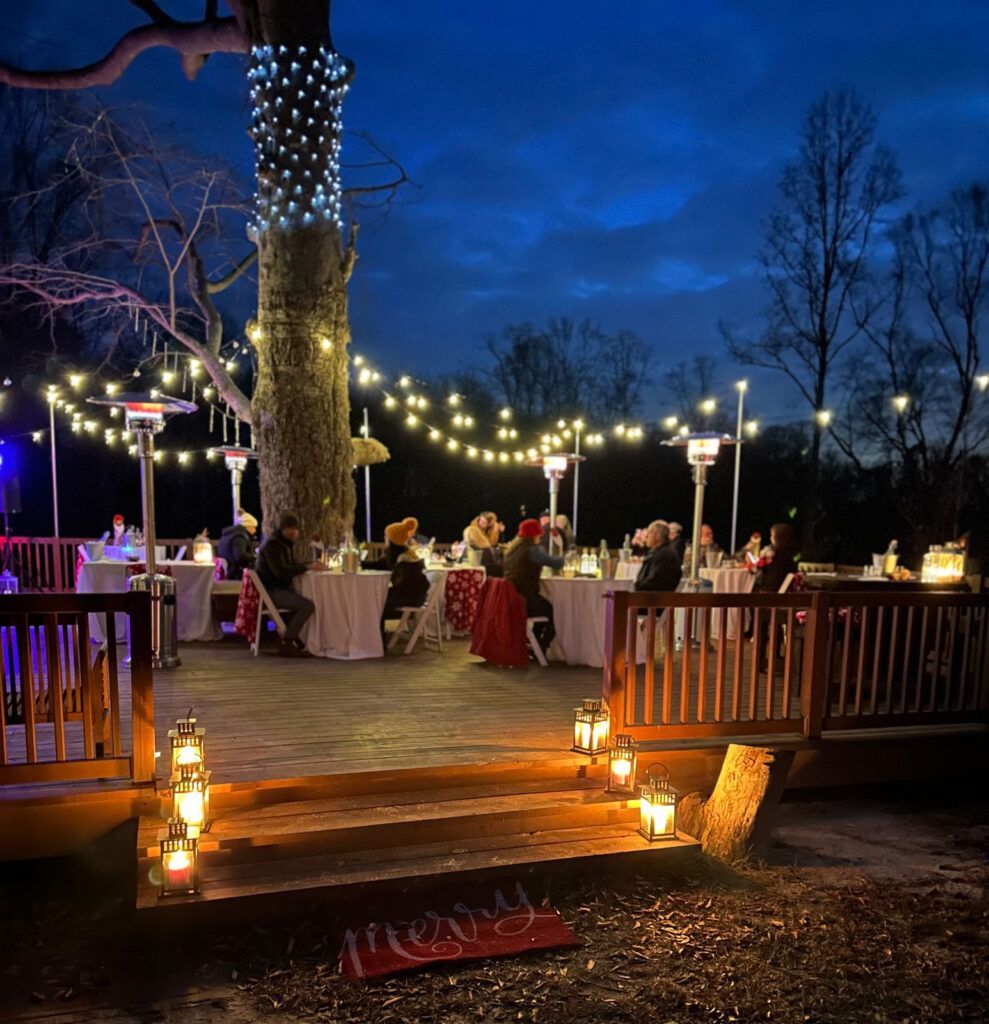 A group of people are sitting at tables on a deck at night.