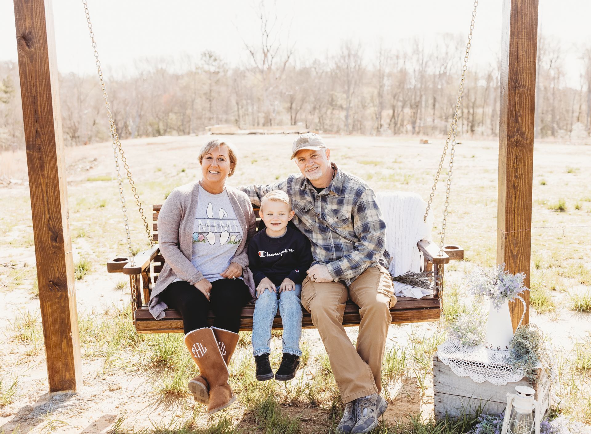 A family is sitting on a wooden swing in a field.