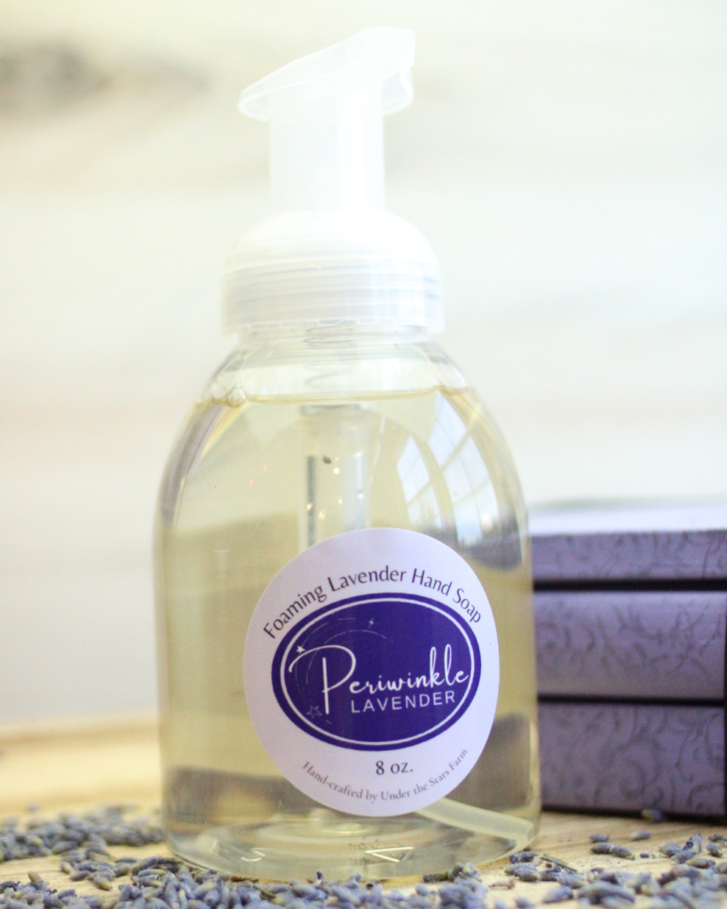 A bottle of foaming lavender soap is sitting on a wooden table.