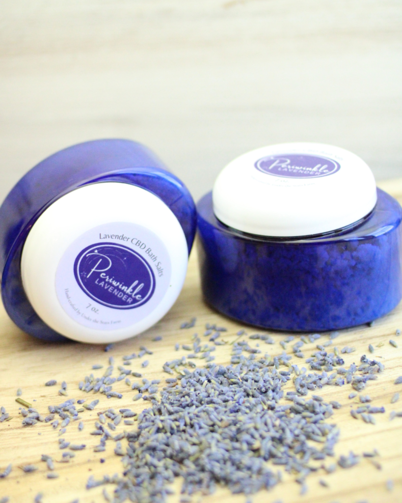 Two jars of powder are sitting on a wooden table surrounded by lavender flowers.