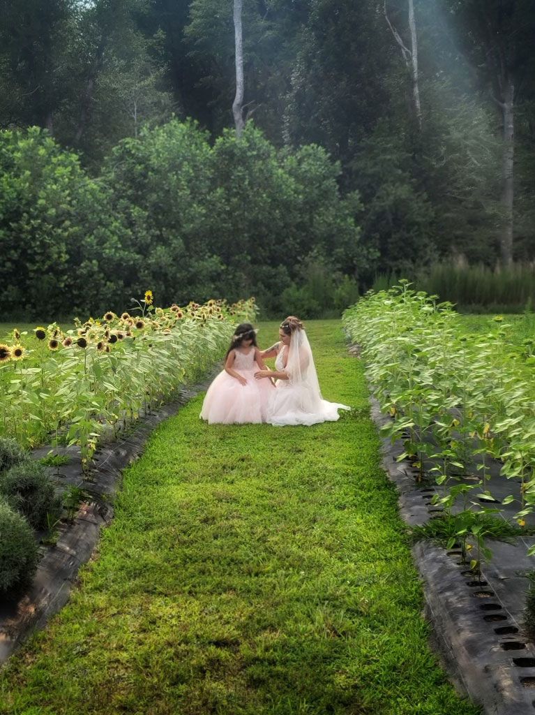 A bride and a flower girl are sitting in a field of sunflowers.