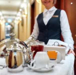 Bandeja de té con tetera de plata, tazas y un camarero sonriente en el pasillo de un restaurante.