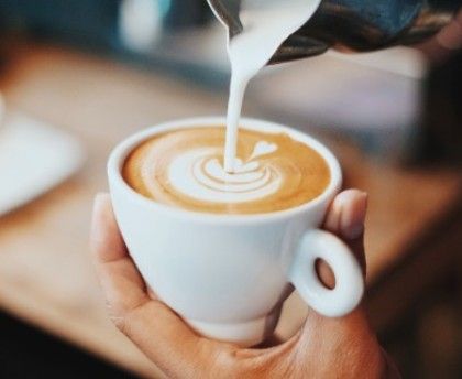 Vertiendo a mano un dibujo de latte en una taza blanca sostenida en una mano.
