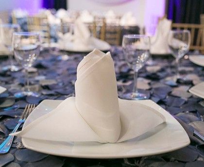 Servilleta blanca doblada sobre un plato blanco en una mesa de comedor formal con decoración de mesa azul.