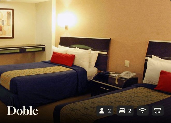 Dos camas dobles con ropa de cama azul marino y almohadas rojas en una habitación de hotel de color beige.