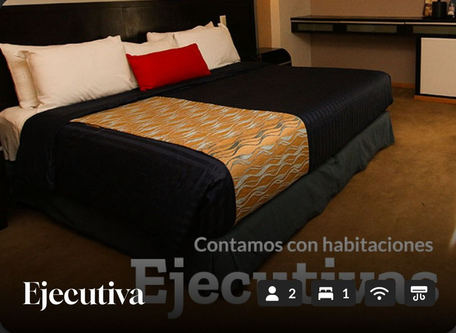Habitación de hotel con una cama king size negra, almohadas blancas y rojas y un camino de mesa estampado.