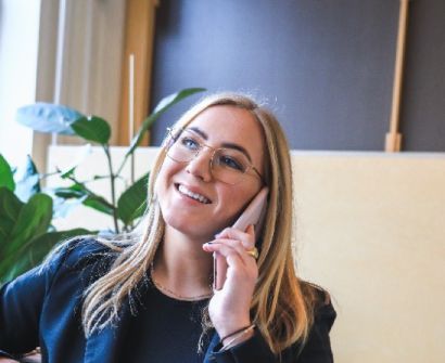 Una persona sonriente hablando por teléfono en una oficina, con una planta y una ventana al fondo.