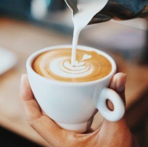 Leche vertida en una taza blanca con arte latte sostenida en la mano