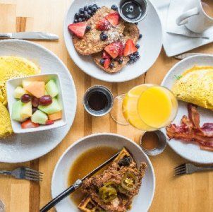 Desayuno servido en una mesa de madera con panqueques, ensalada de frutas, huevos, tocino, café y jugo de naranja.