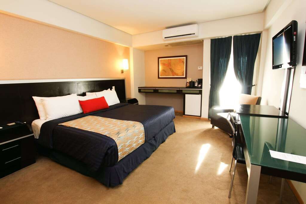 Habitación de hotel moderna con dos camas, iluminación cálida y un escritorio junto a la ventana.