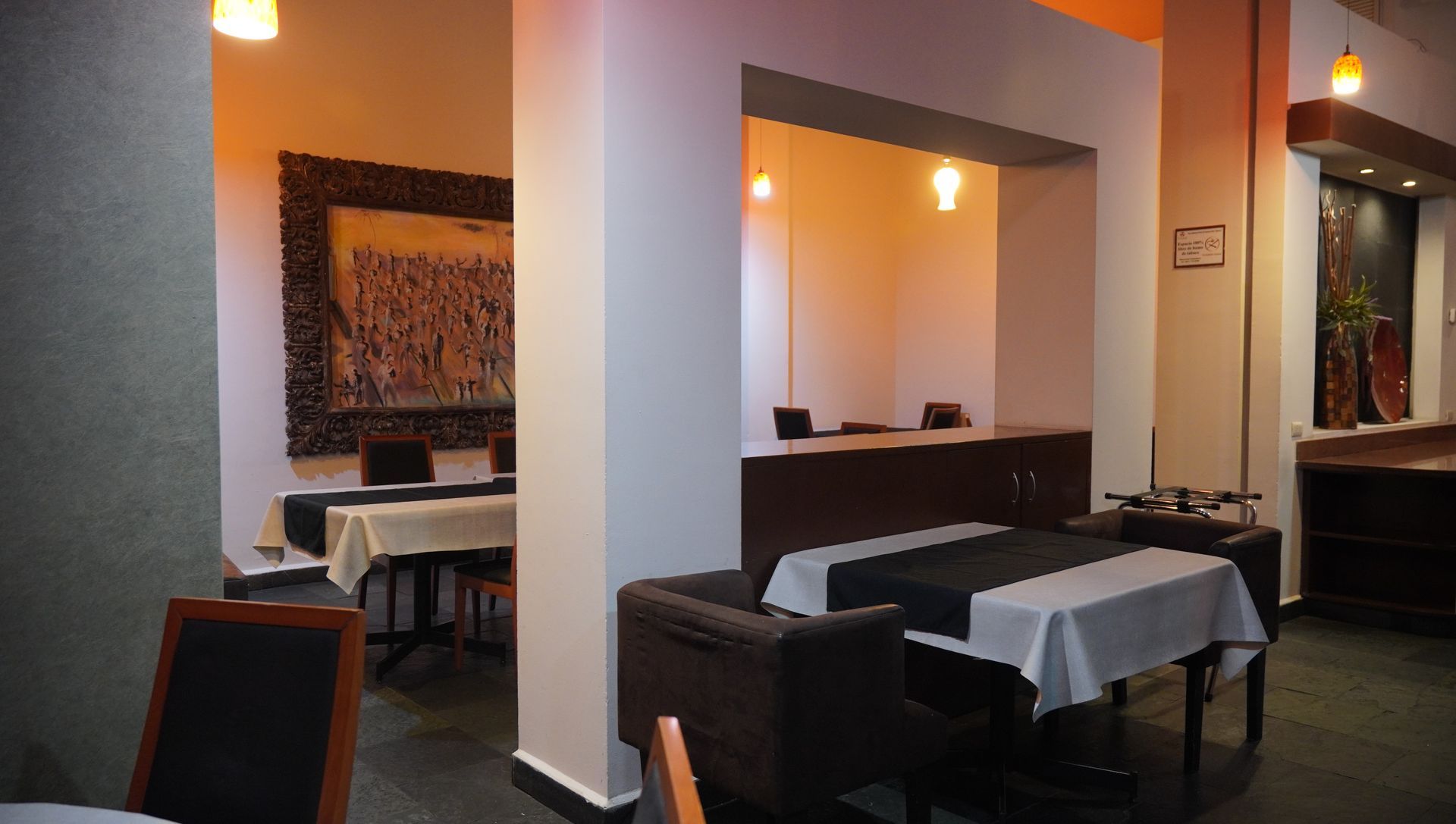 Comedor de restaurante moderno con cabinas oscuras, manteles blancos y luces de pared cálidas.