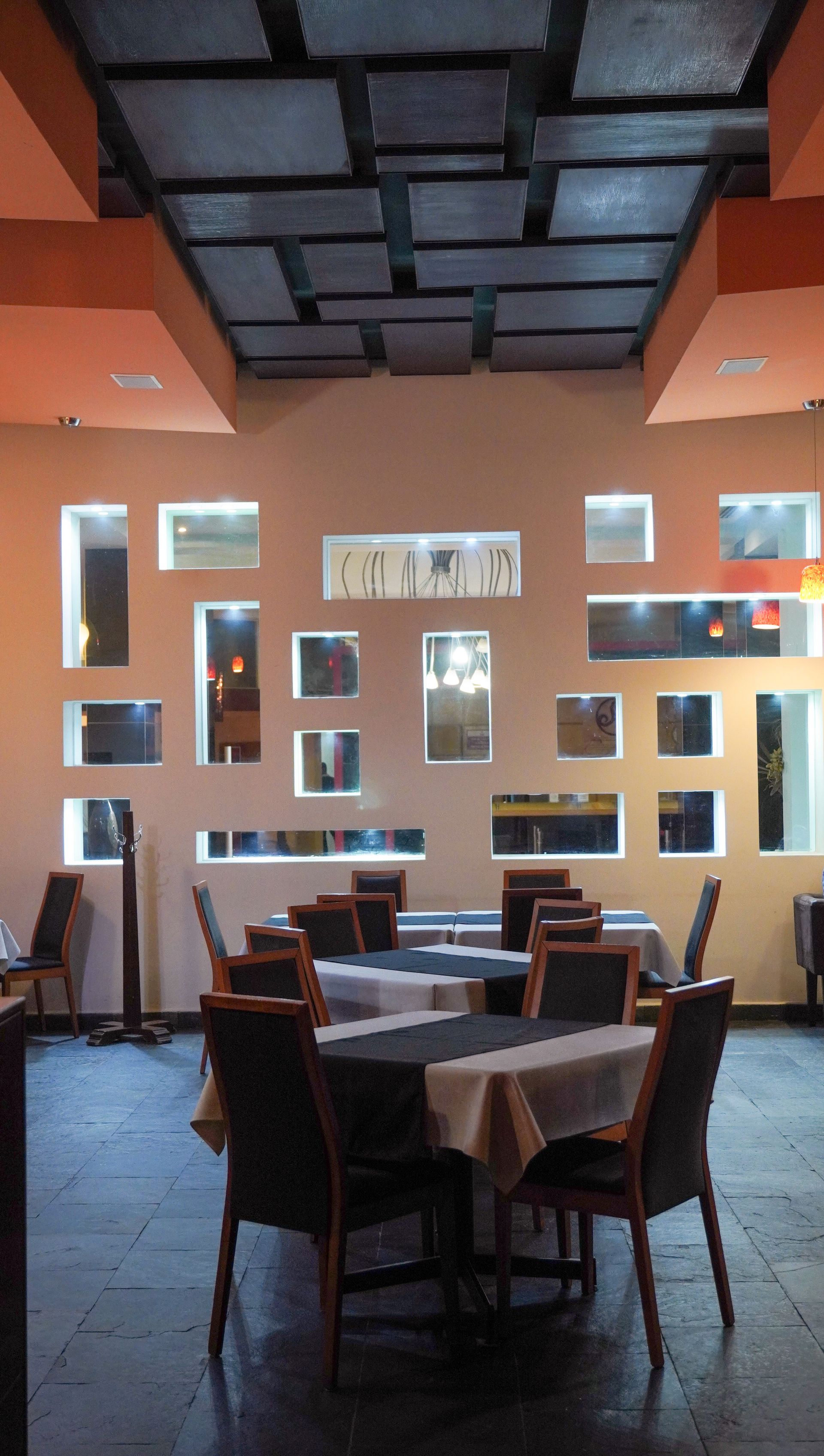 Comedor vacío de un restaurante con mesas y sillas, paredes de color naranja cálido y techo estampado.
