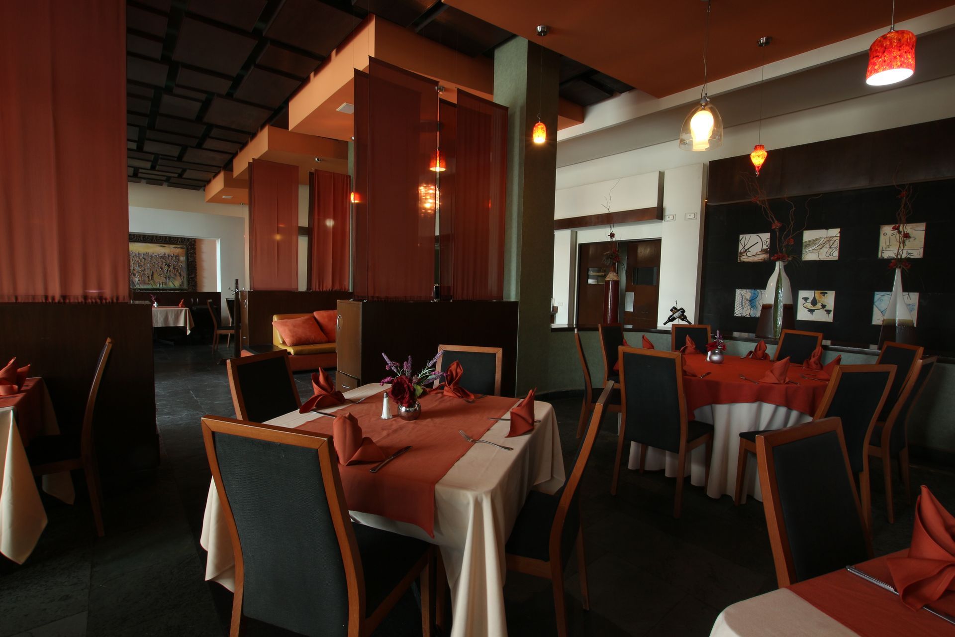 Elegante comedor de restaurante con manteles rojos, sillas oscuras y cálida iluminación colgante.