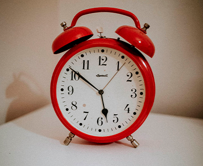 Reloj despertador rojo de doble campana sobre fondo blanco, marcando aproximadamente las 6:50.