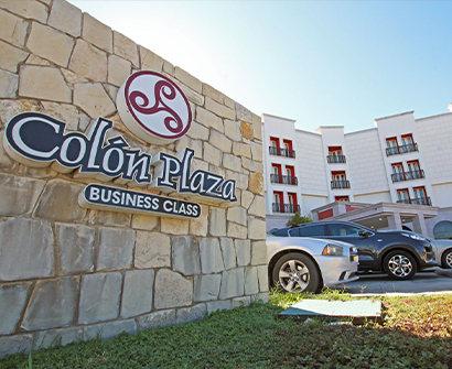 Letrero de Colón Plaza Business Class junto a autos estacionados y un edificio de hotel bajo un cielo azul