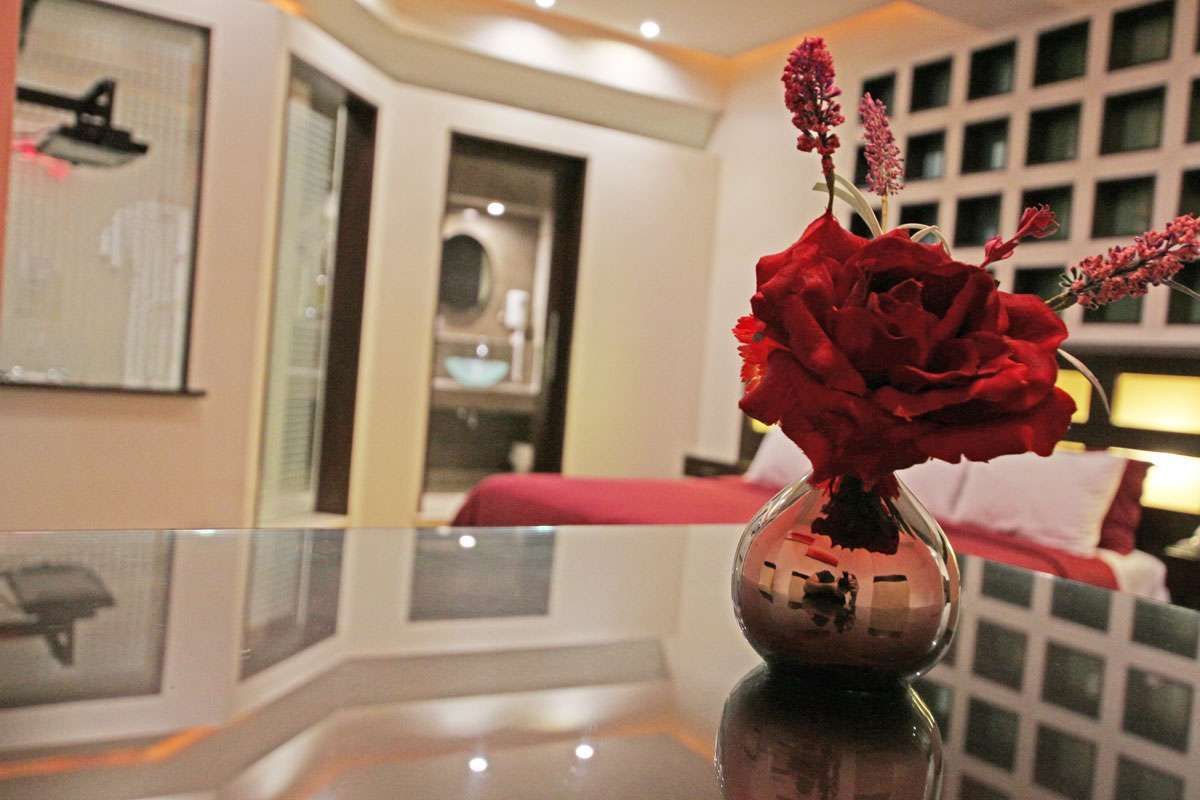 Rosas rojas en un jarrón sobre una mesa reflectante en una habitación con iluminación tenue.