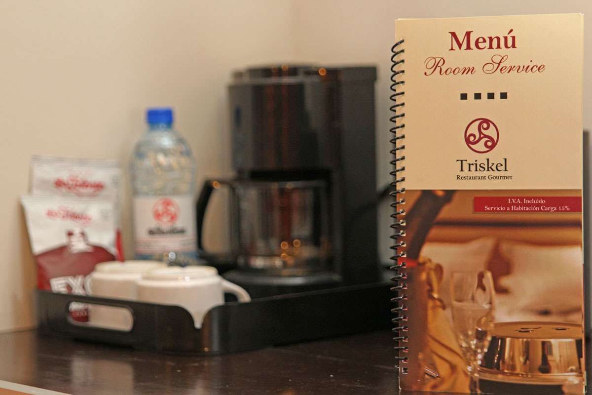 Estación de café con cartel de menú, agua embotellada, servilletas y una cafetera sobre un mostrador.