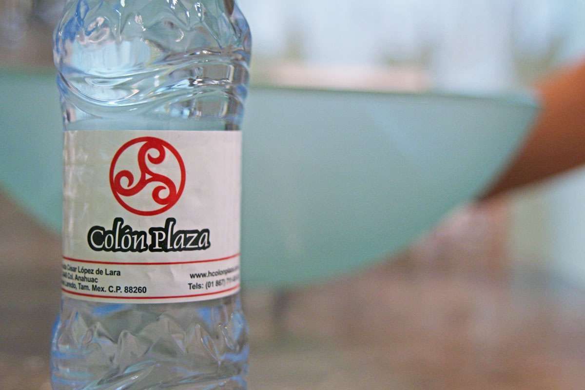 Botella de agua con la etiqueta “Colon Plaza” frente a un cuenco azul borroso sobre una mesa.