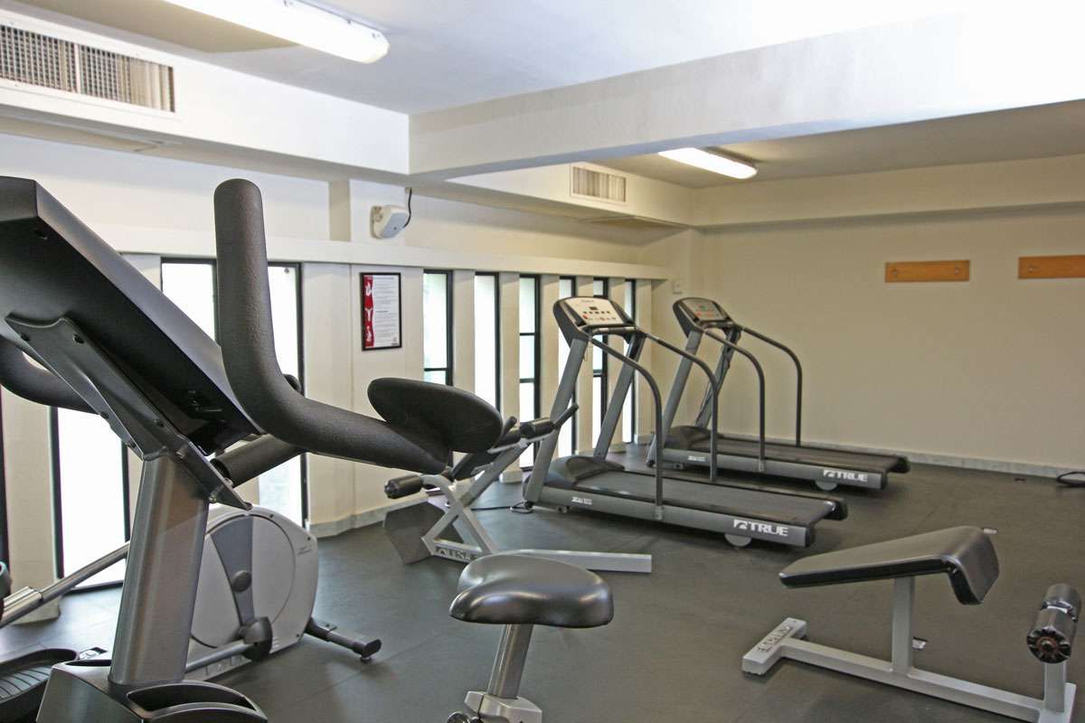 Gimnasio vacío con cinta de correr, banco de pesas y máquinas de ejercicio bajo luces fluorescentes.