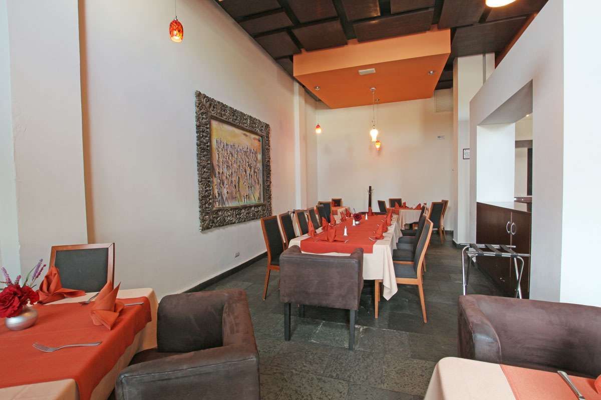 Tranquilo comedor de restaurante con manteles rojos, sillas tapizadas y arte en las paredes.