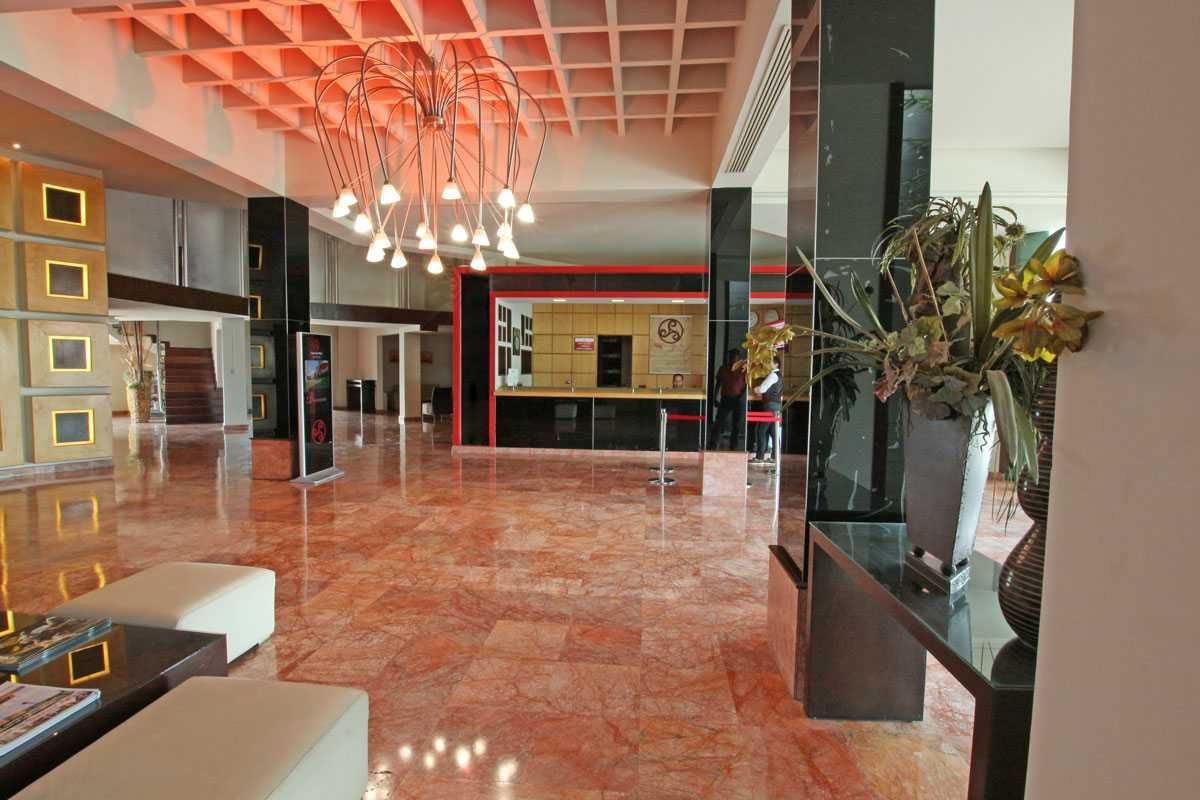 Vestíbulo de hotel moderno con suelos rojos brillantes, lámparas de araña y un arreglo floral decorativo.