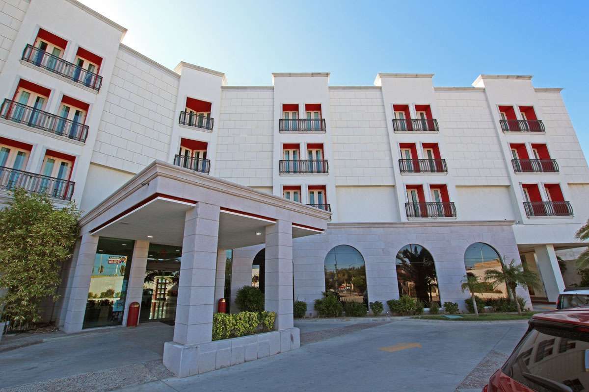 Edificio moderno de color blanco con balcones rojos y ventanas arqueadas en la planta baja, junto a la entrada para vehículos.