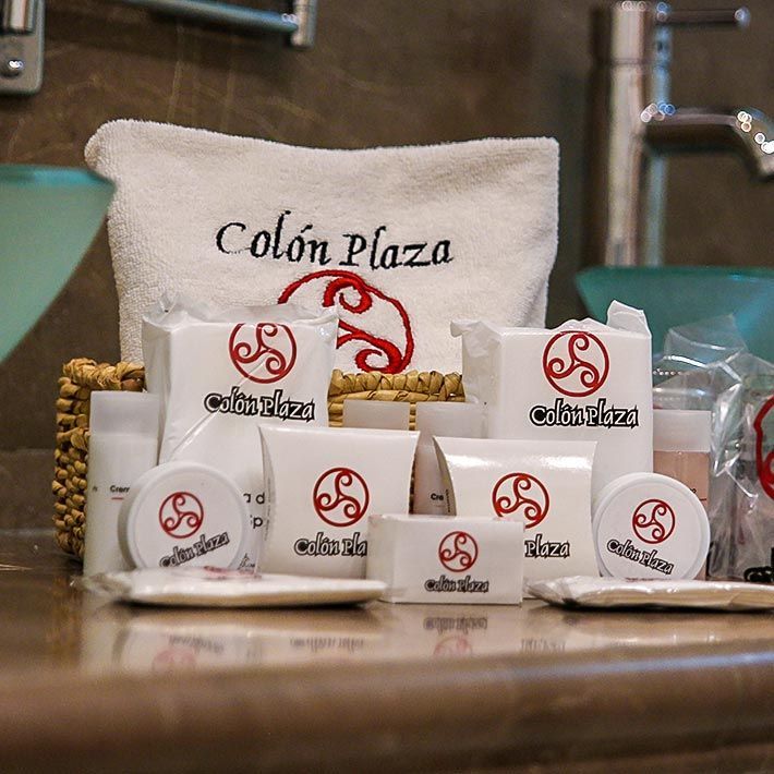 Accesorios blancos de marca y una bolsa de tela con la etiqueta “Colón Plaza” sobre un mostrador de madera.