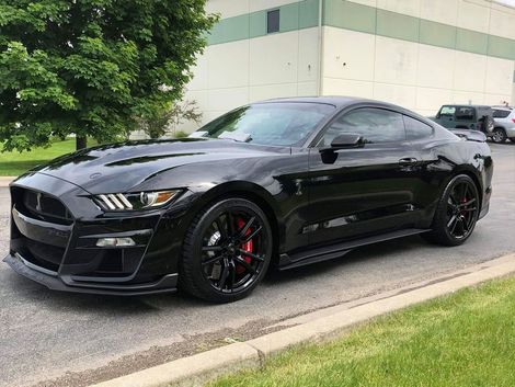 Black Ford Shelby GT500 sports car parked on asphalt, red brake calipers visible, near a building.