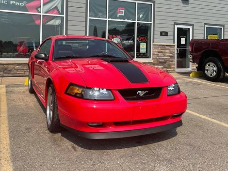 Red Ford Mustang with black racing stripe parked outside a building.