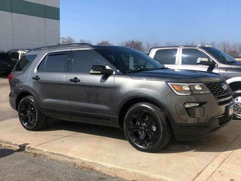 Gray Ford Explorer with black wheels parked on a sidewalk.