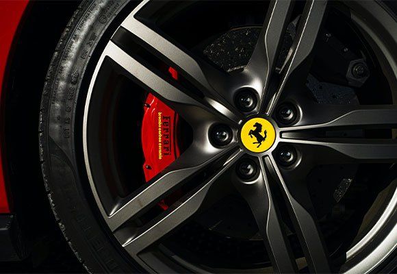 Black Ferrari wheel with red brake caliper and yellow logo.