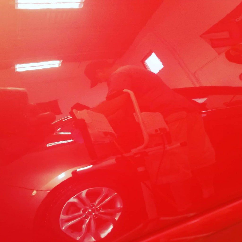 Man working on a car in a garage, illuminated by red light.