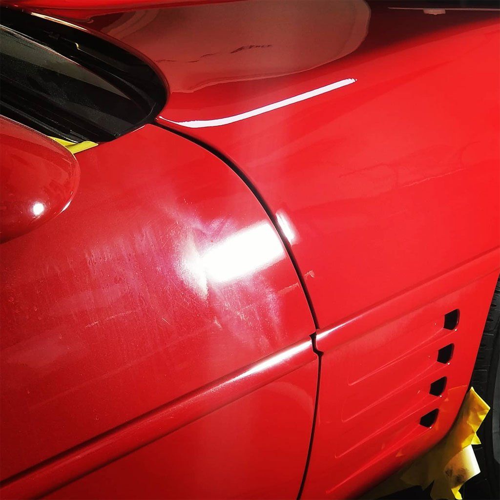 Red car door with scratches, reflecting light. Close-up, showing details.