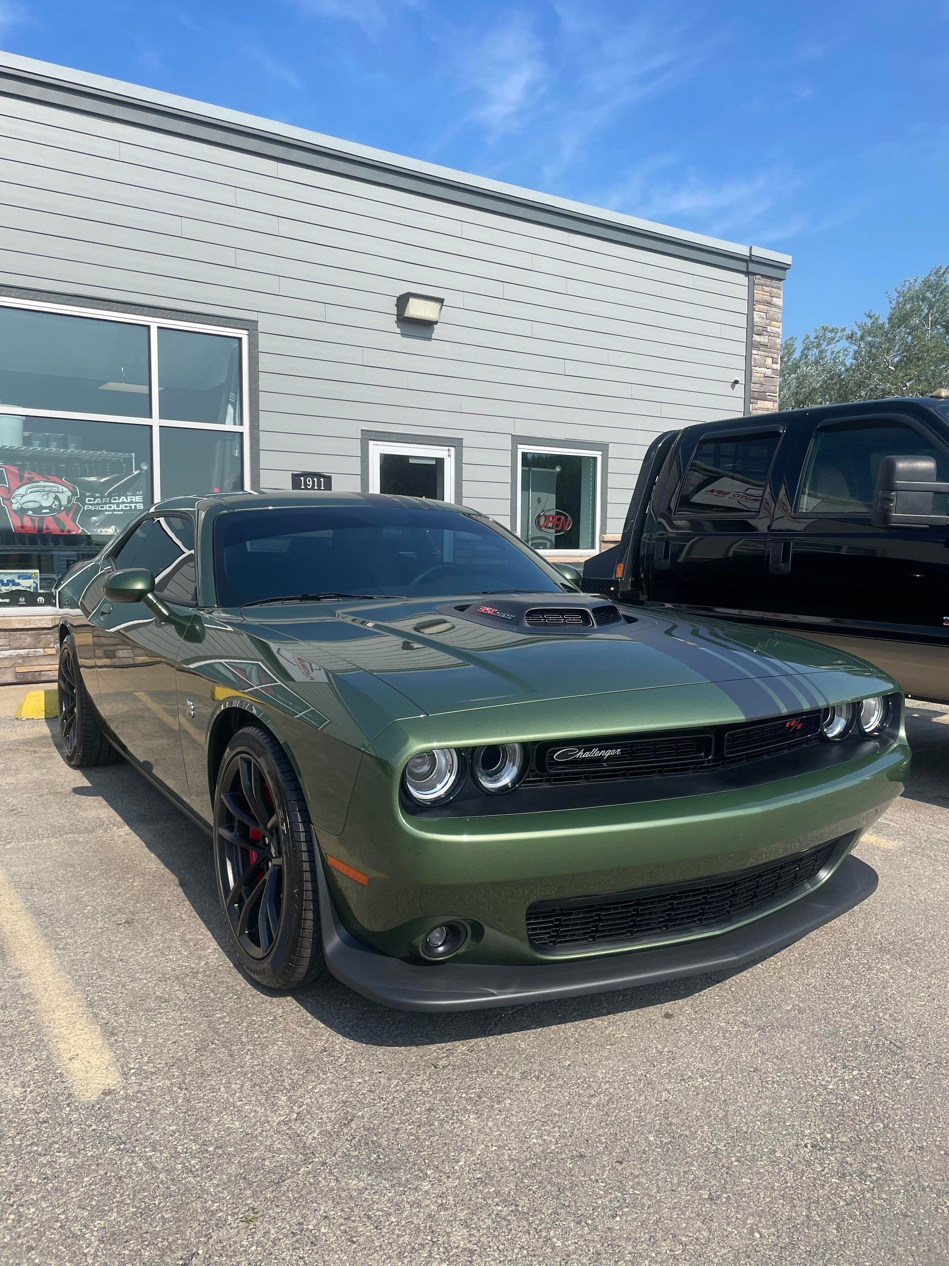 Green Dodge Challenger with black racing stripes parked outside a building on a sunny day.
