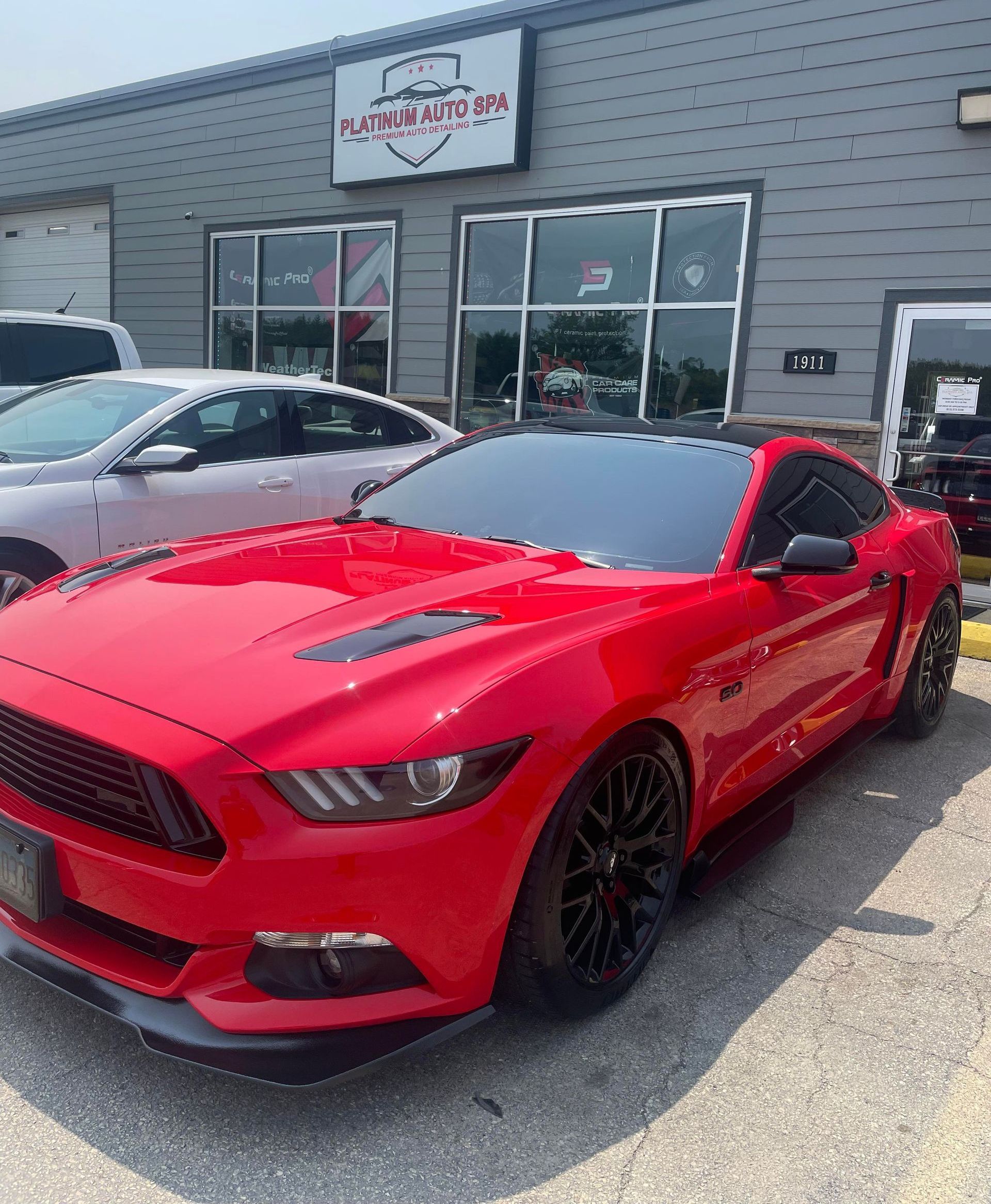 Red Mustang sports car parked outside a car detailing shop with tinted windows.