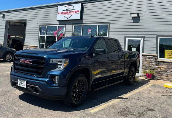 Blue GMC Sierra truck parked in front of a building with a business sign, sunny day.