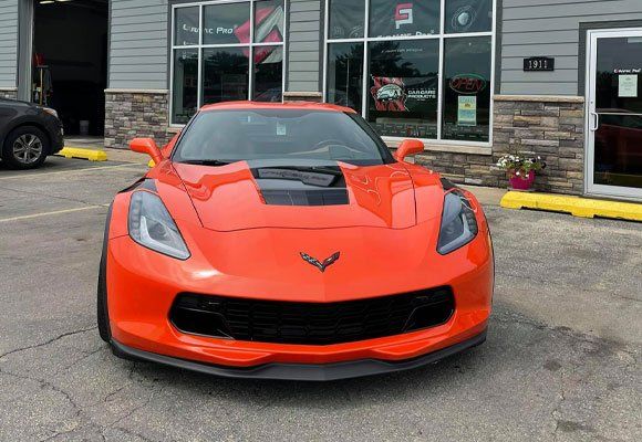 Bright orange Corvette parked in front of an auto shop.