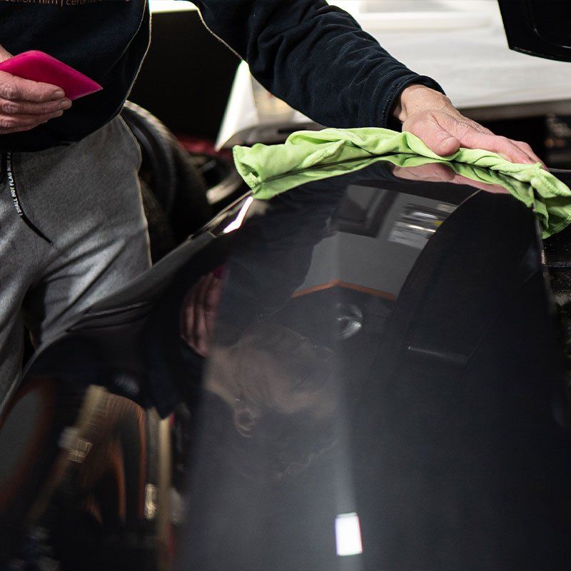 Person wiping a dark car surface with a green cloth, holding a pink tool.