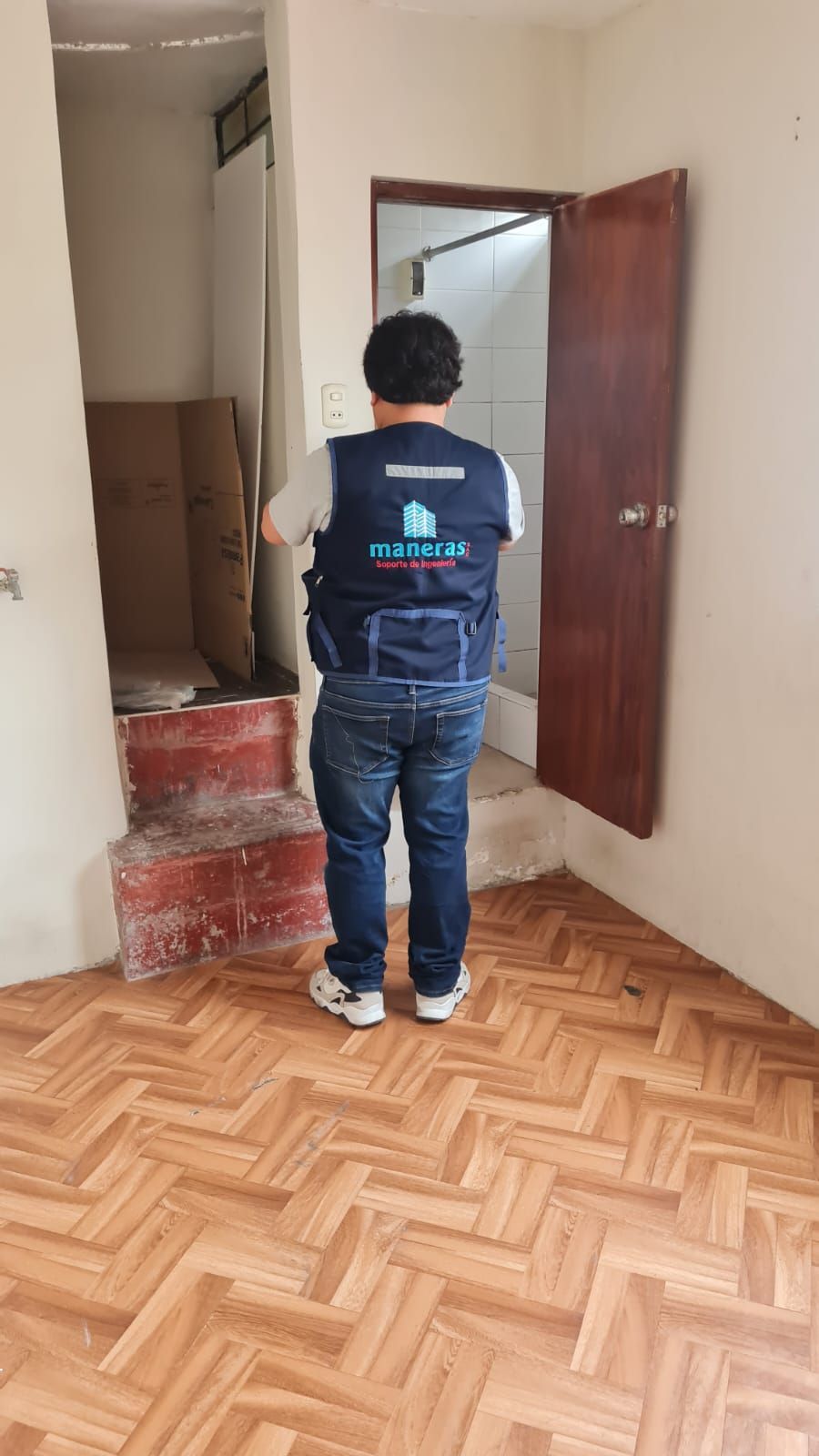 Persona de pie en un pasillo cerca de una puerta abierta y unas escaleras con baldosas rojas
