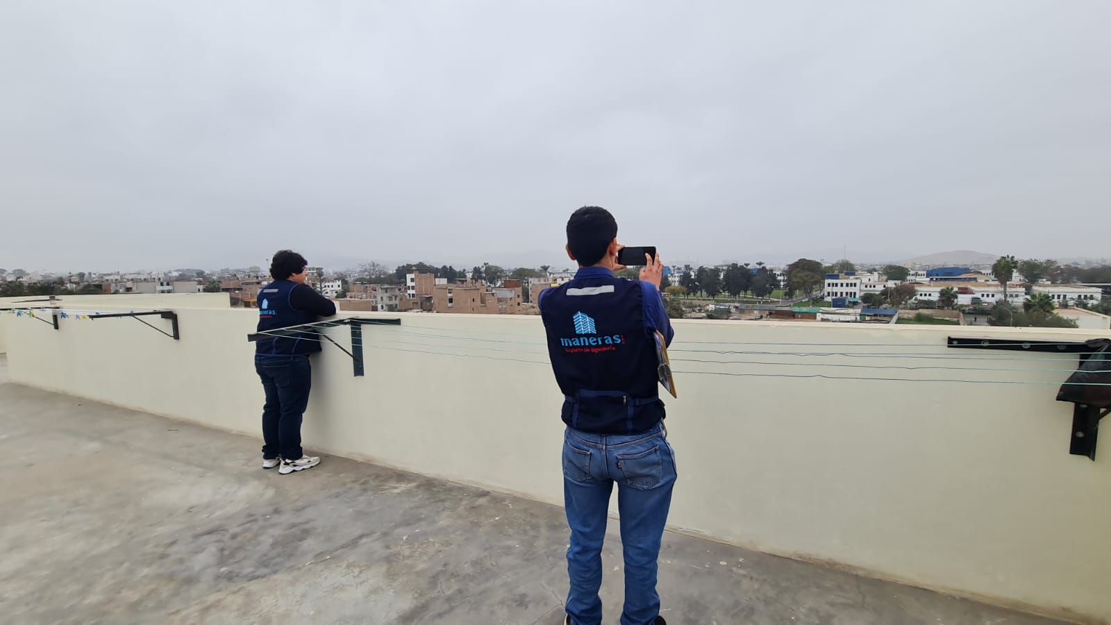 Dos personas con chalecos oscuros fotografían un río ancho desde un paseo fluvial de hormigón.