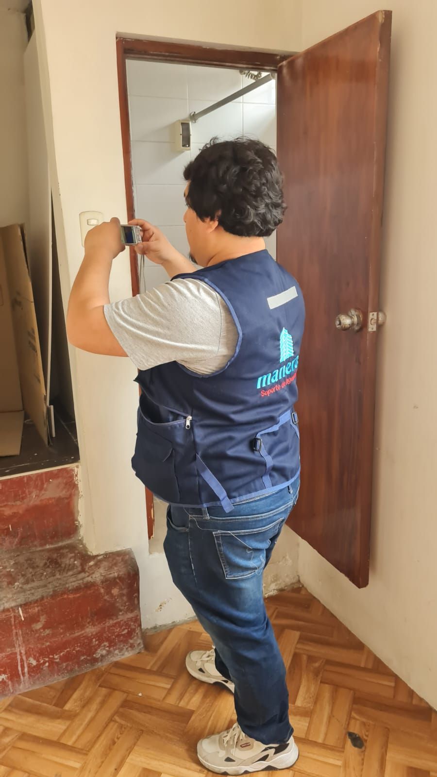 Persona que mide el marco de una puerta con una cinta métrica en un pasillo, vestida con un chaleco azul