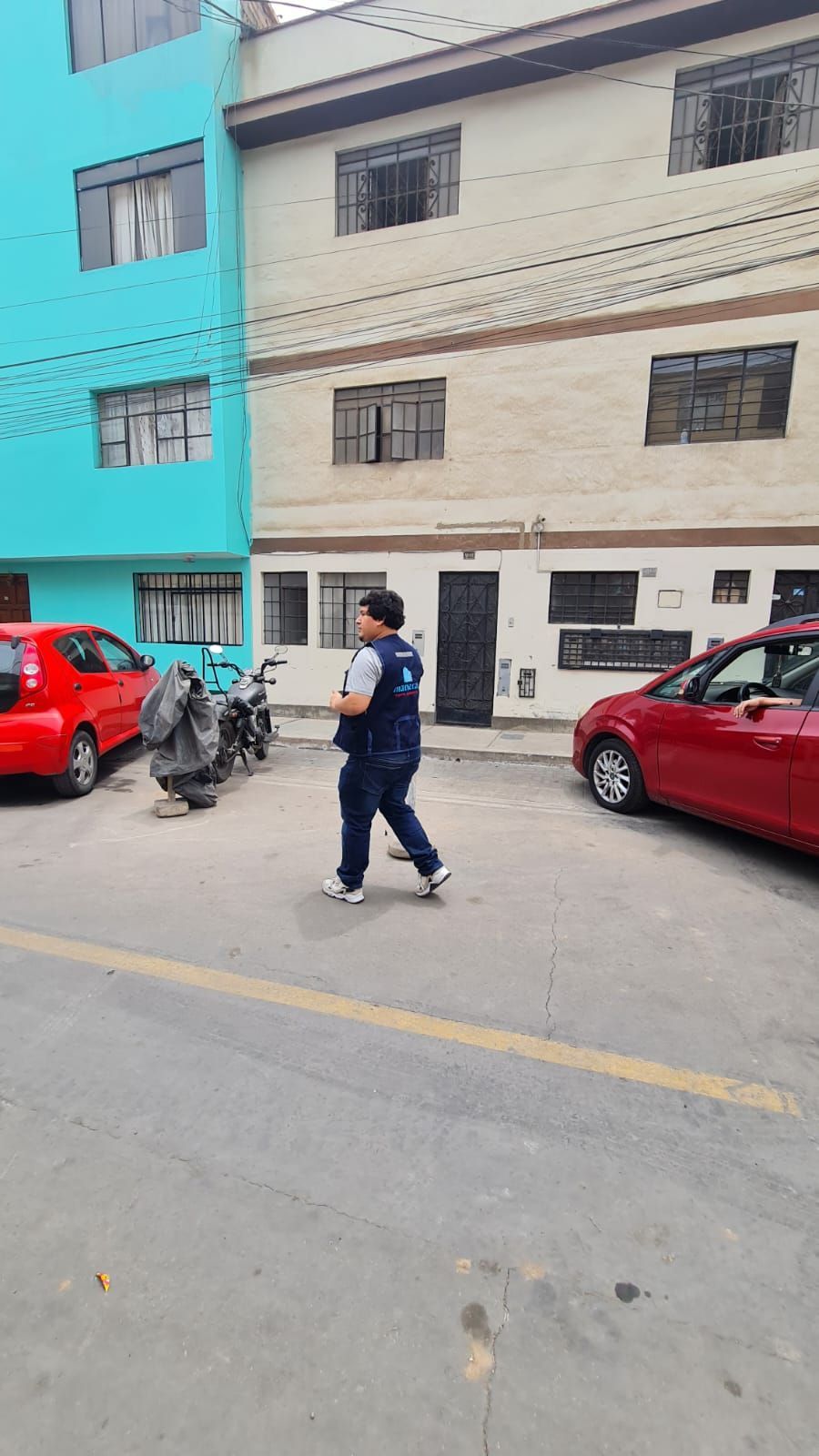 Una persona camina por una calle junto a coches aparcados y un edificio de varias plantas