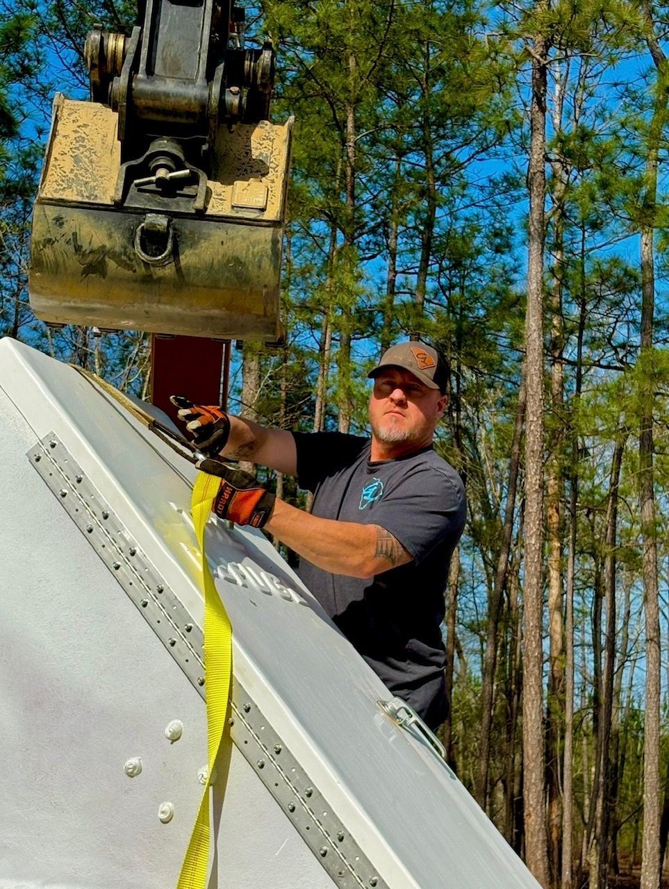 Worker in safety gear securing a large white panel with a crane in a wooded area