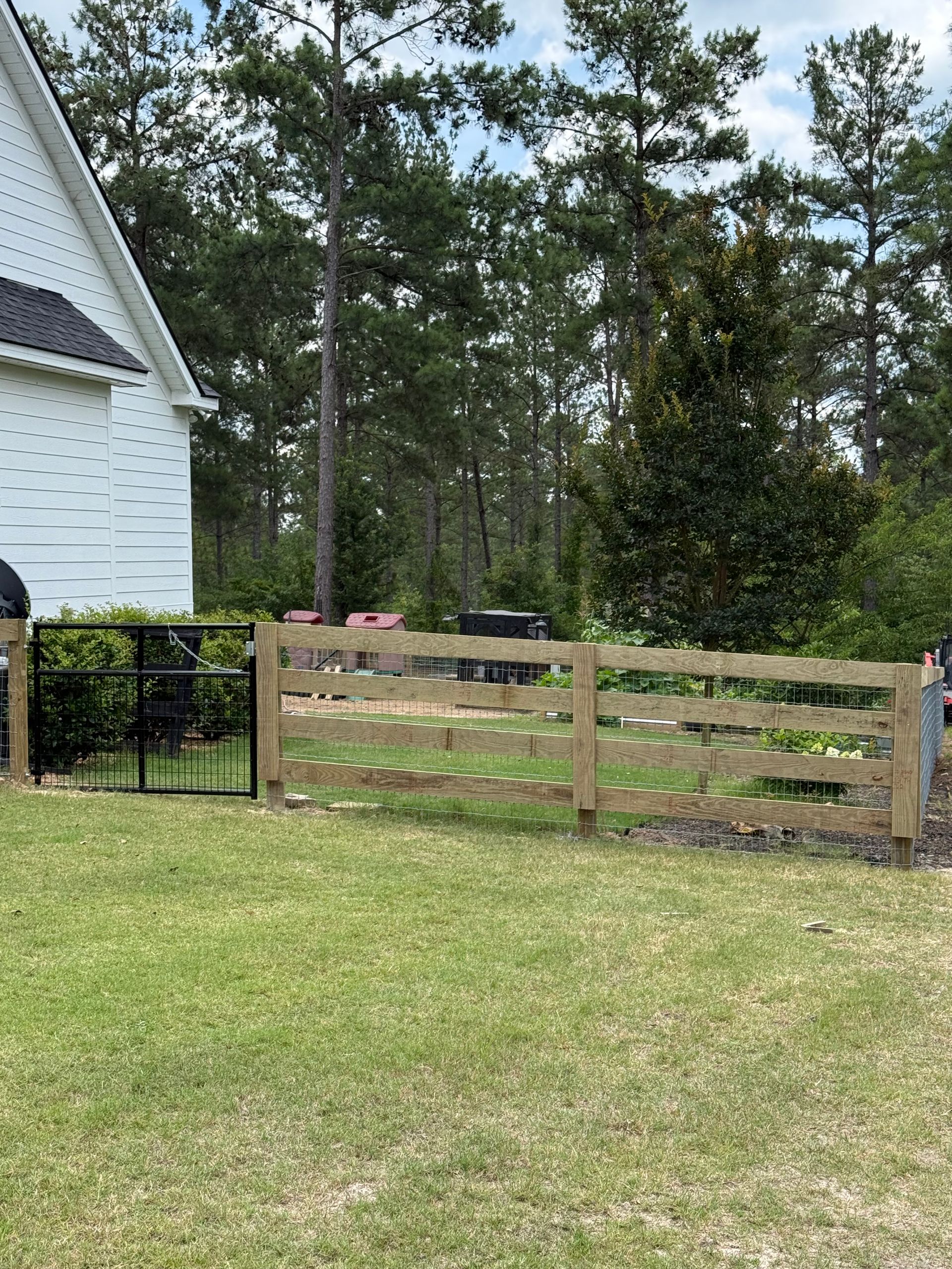 Red skid steer and black pickup truck by a black metal gate in a wooded yard.