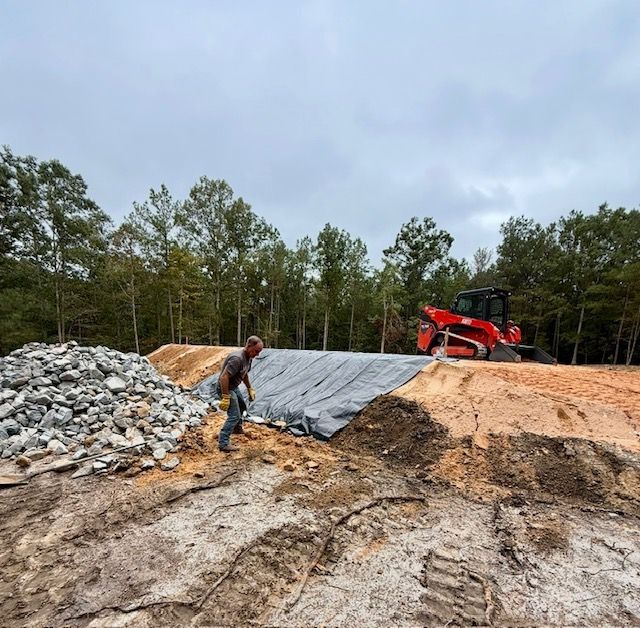 Construction site with a worker, gravel pile, and orange skid steer on a dirt slope