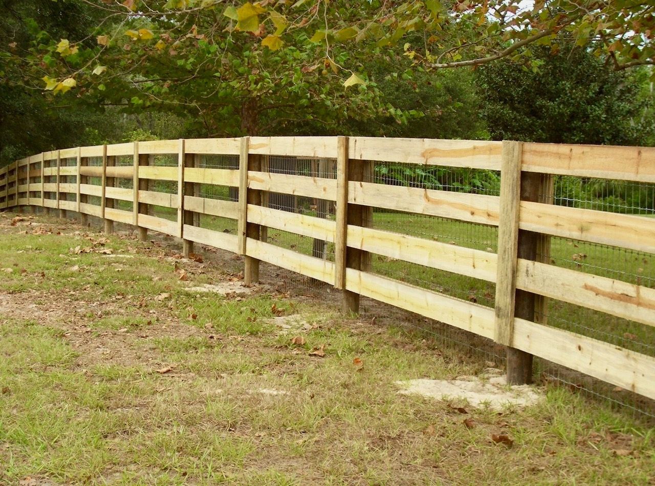 Wooden fence curving through a grassy yard with trees in the background