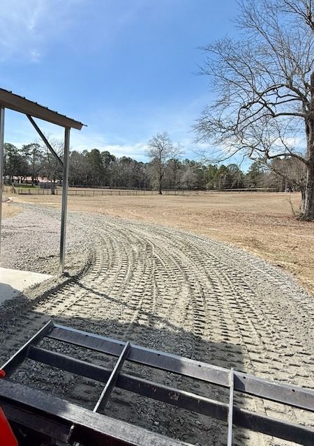 Gravel path curving through a bare field under a blue sky, viewed from a porch or deck