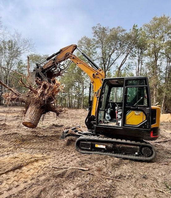 Yellow excavator lifting a large tree stump in a cleared wooded area
