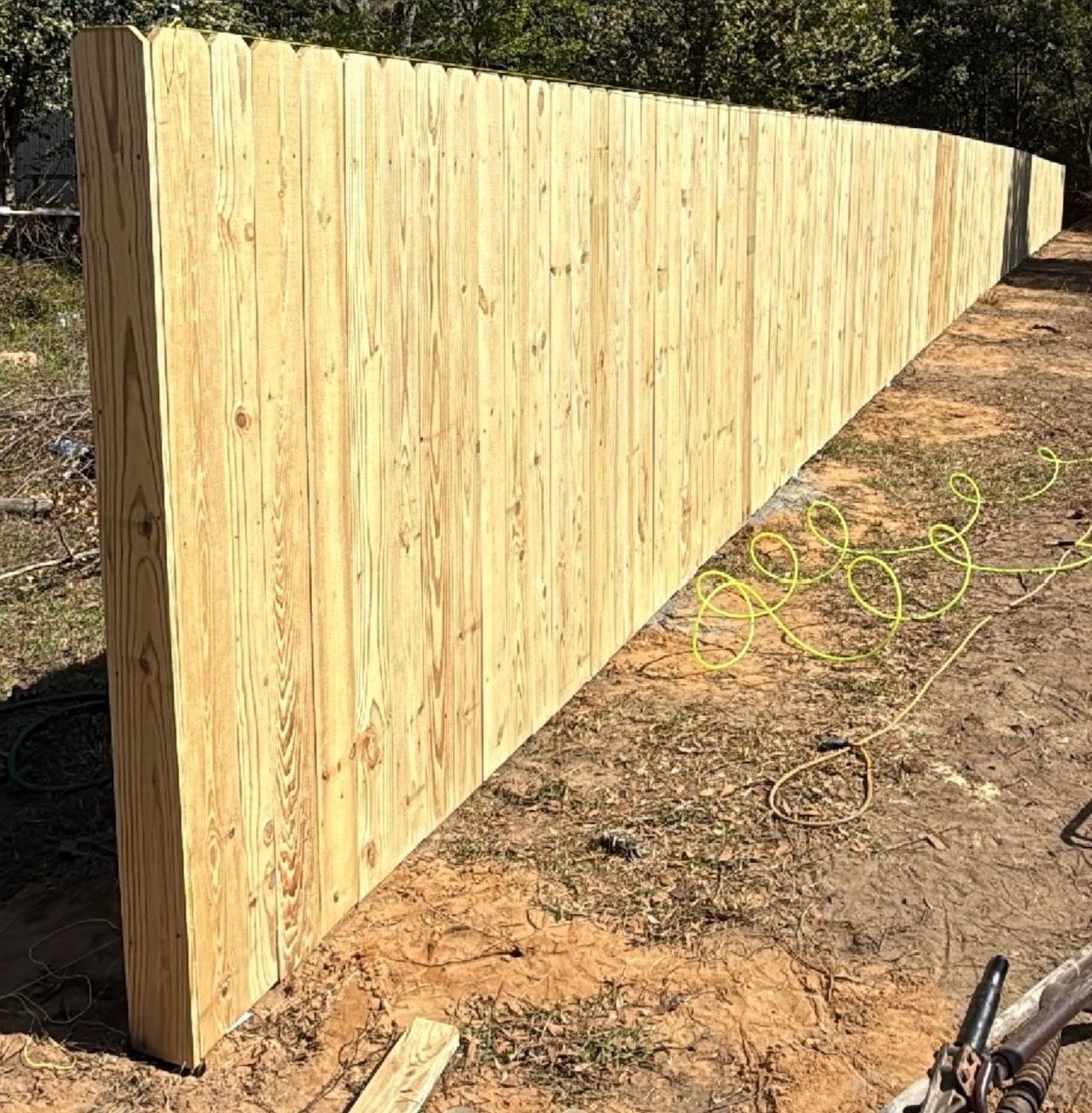 New wooden fence panels along a dirt yard beside trees