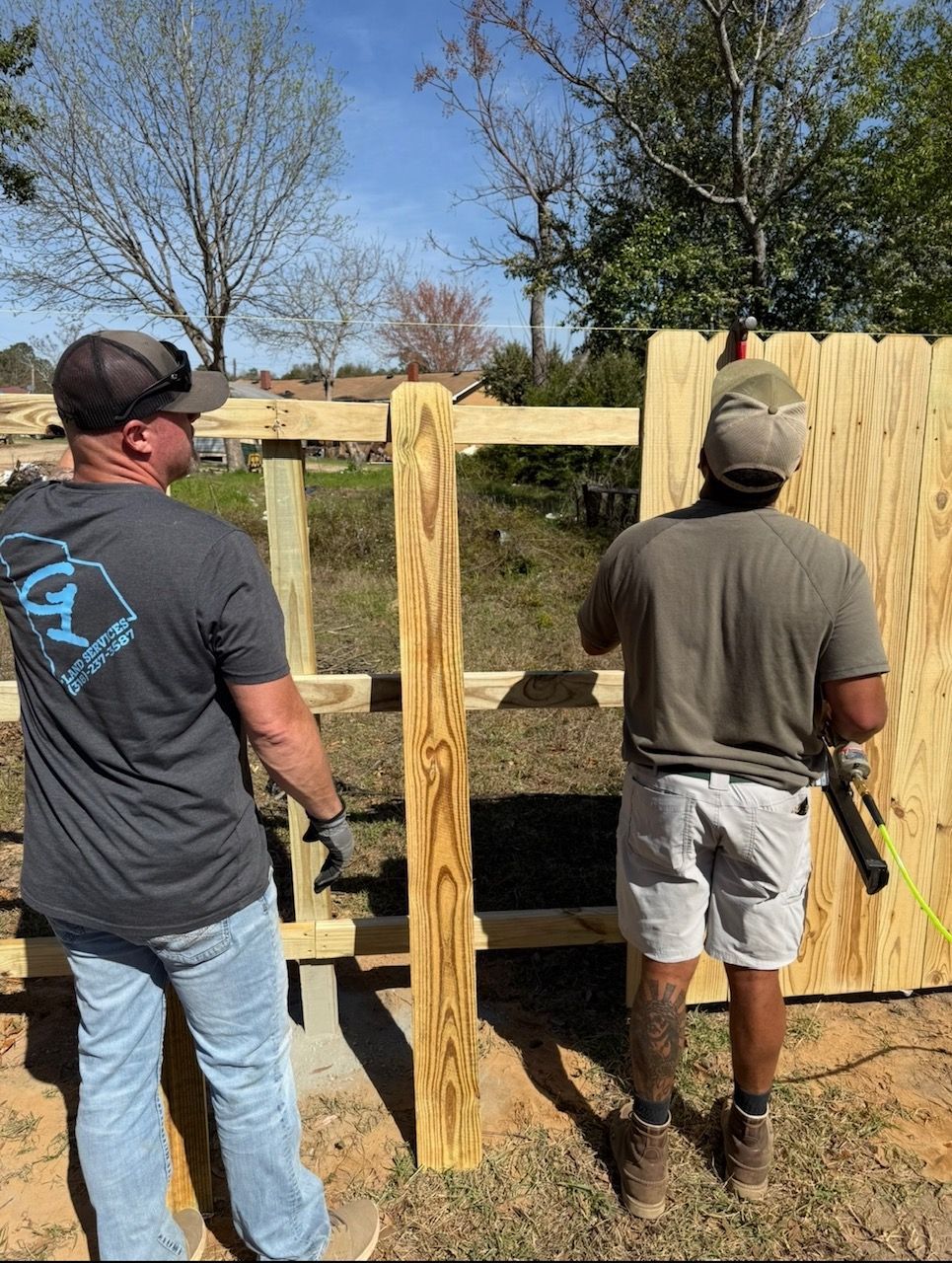 Two people building a wooden fence outdoors on a sunny day